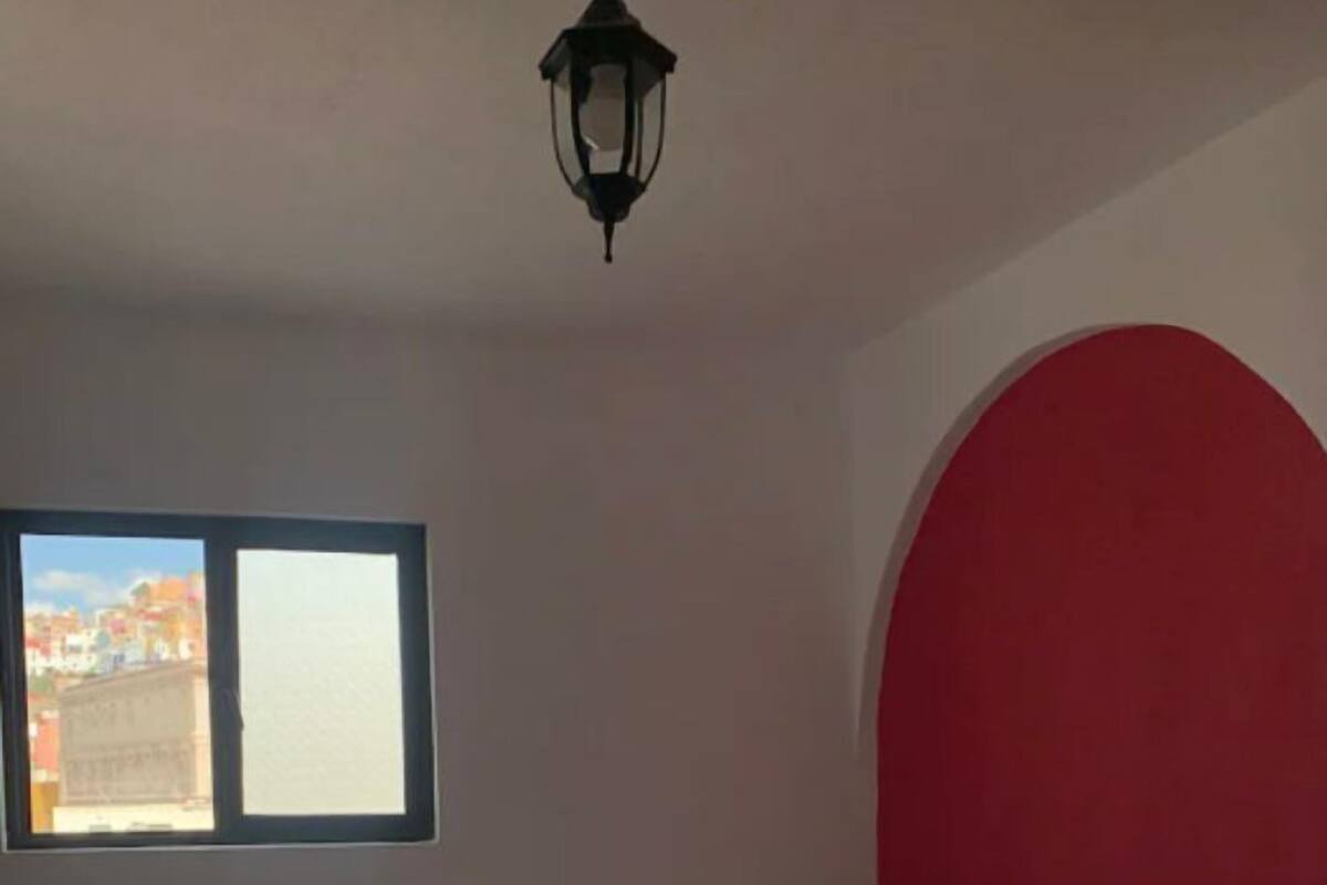 Une chambre avec deux lits, une fenêtre et une arche rouge.