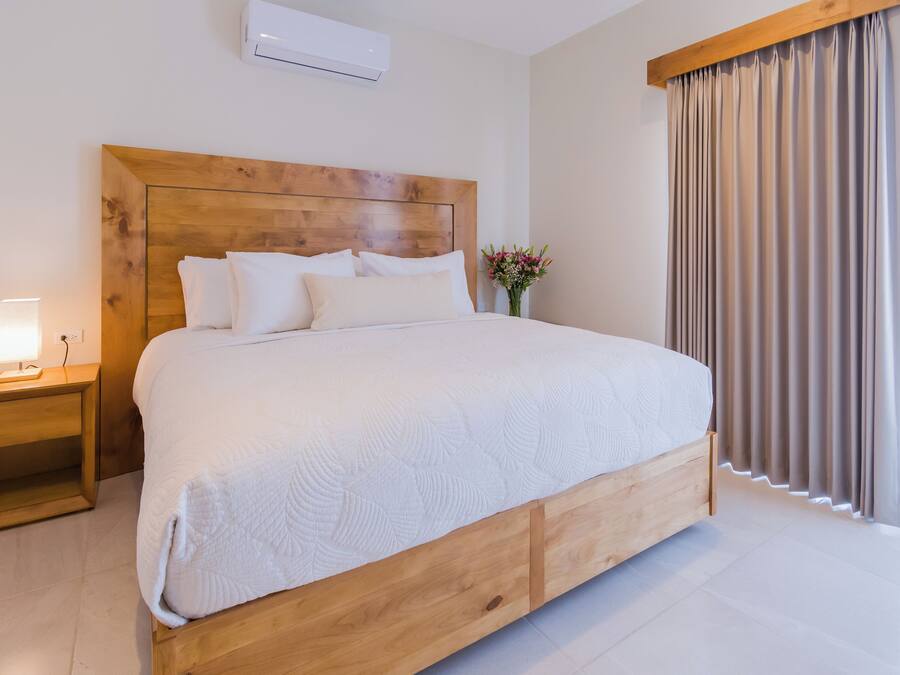 A neatly made bed with a wooden headboard, a bedside table with a lamp, and a window with curtains.