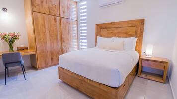 A bedroom with a wooden bed, a desk with a chair, and a nightstand with a lamp.