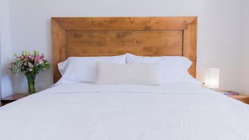 Una cama grande con cabecera de madera, ropa de cama blanca y una mesita de noche con una lámpara y un libro.