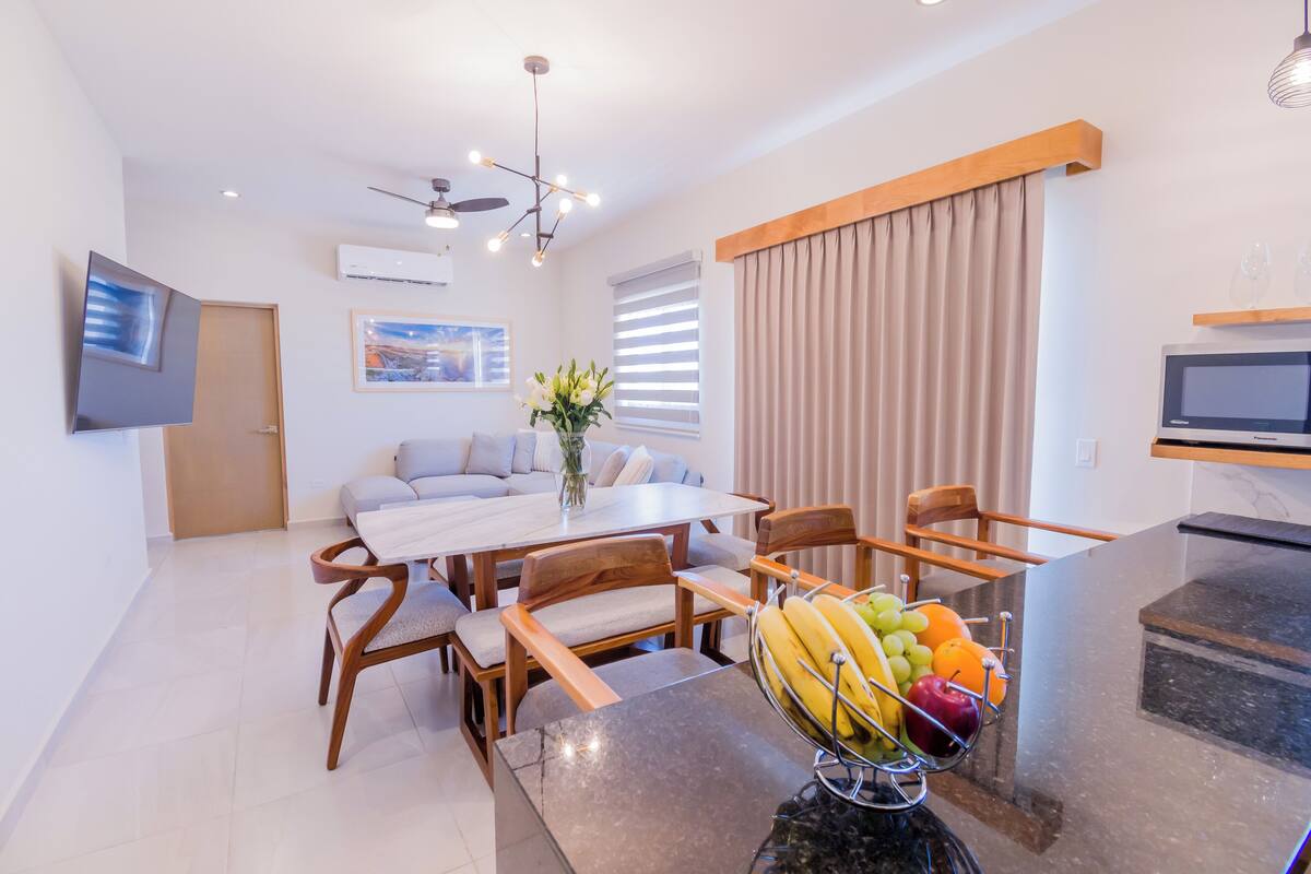 A modern kitchen with a microwave, a dining table with chairs, and a fruit bowl on the counter.