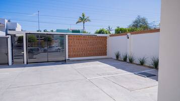 A gated parking area with a concrete floor, a brick wall, and a metal gate.
