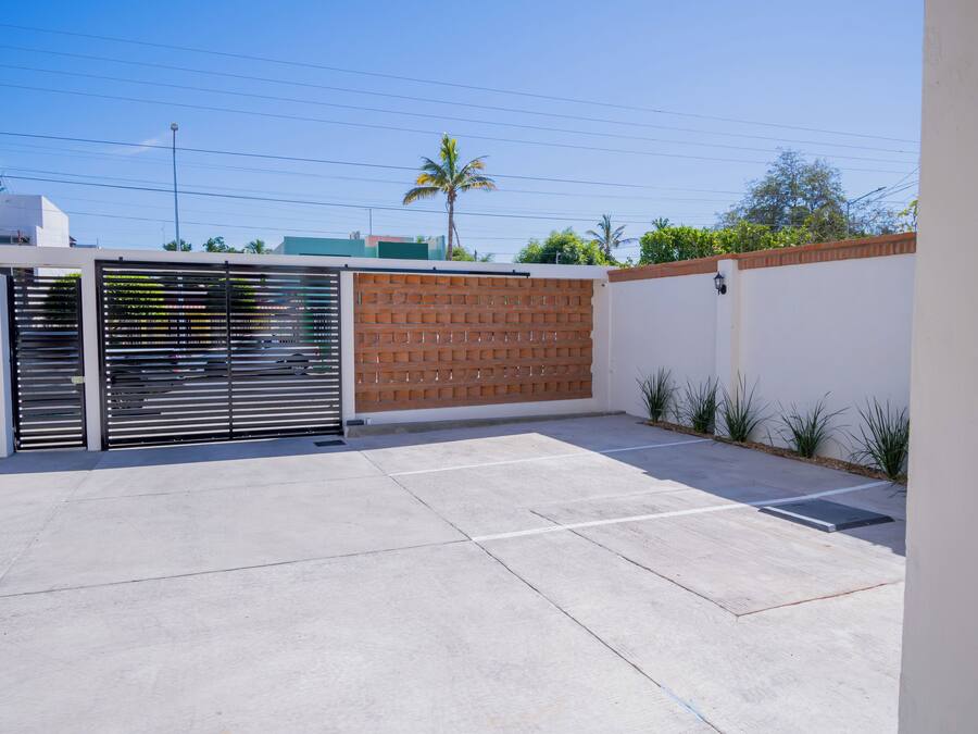 A gated parking area with a concrete floor, a brick wall, and a metal gate.