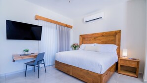 Une chambre avec un lit en bois, un bureau avec une chaise, un téléviseur fixé au mur et un appareil de climatisation.