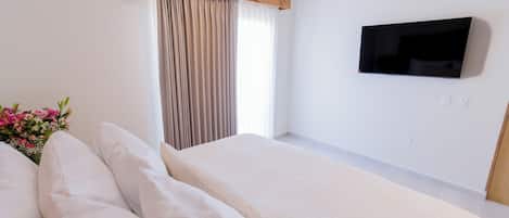 Habitación de hotel con una cama grande, un televisor de pantalla plana en la pared y una ventana con cortinas.