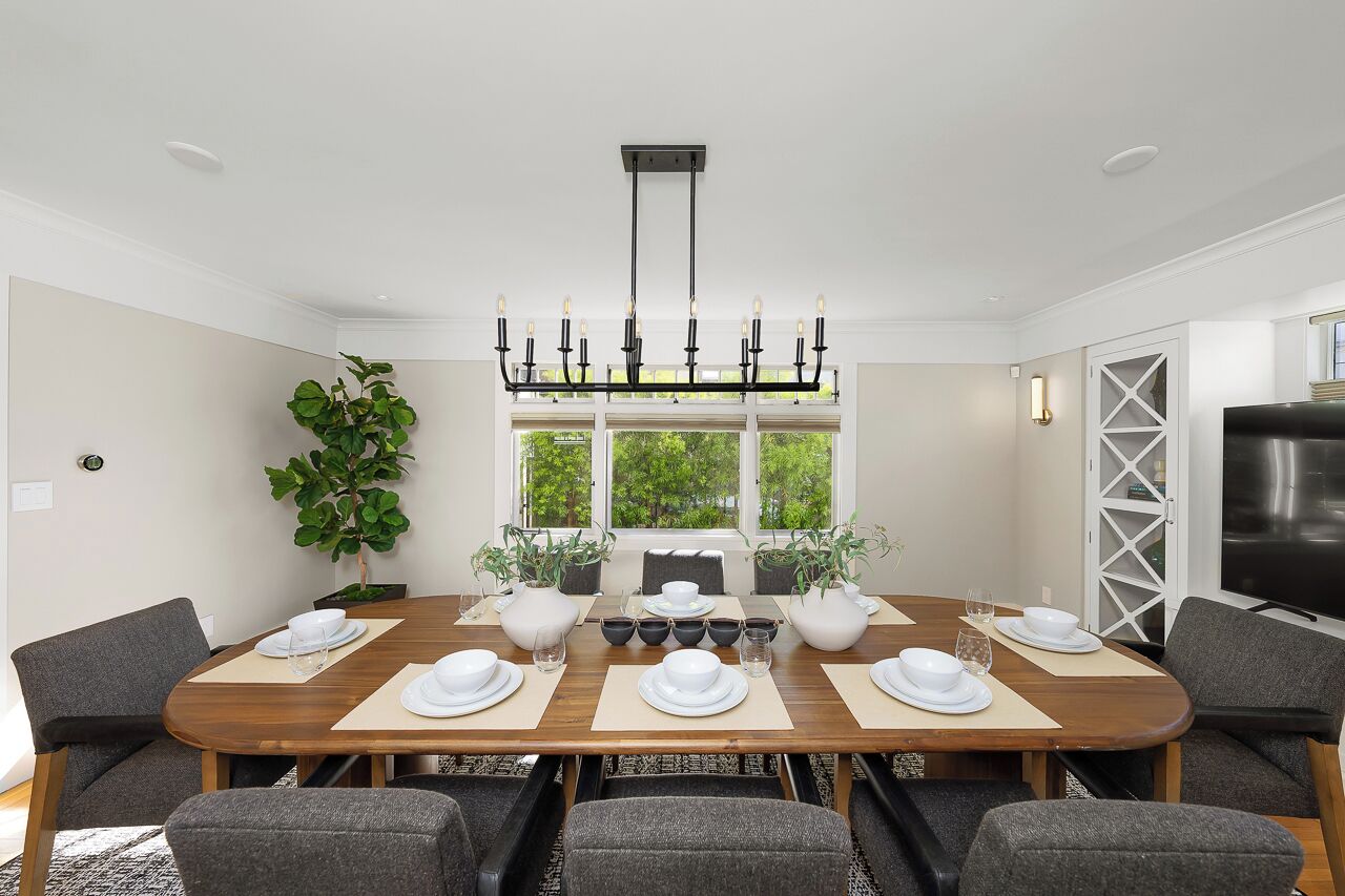 A dining room with a large wooden table set for six, surrounded by grey upholstered chairs.