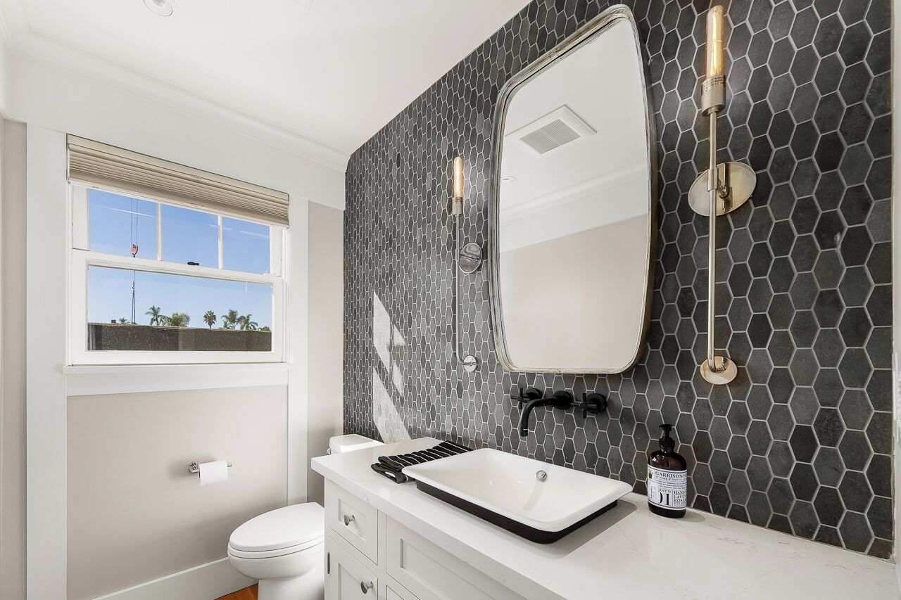 Un baño moderno con un tocador blanco, un espejo grande y un salpicadero de azulejos hexagonales negros.