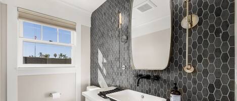 Un baño moderno con un tocador blanco, un espejo grande y un salpicadero de azulejos hexagonales negros.