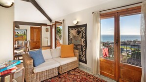 Una habitación con sofá de mimbre, alfombra estampada, vista al mar y techo de madera.
