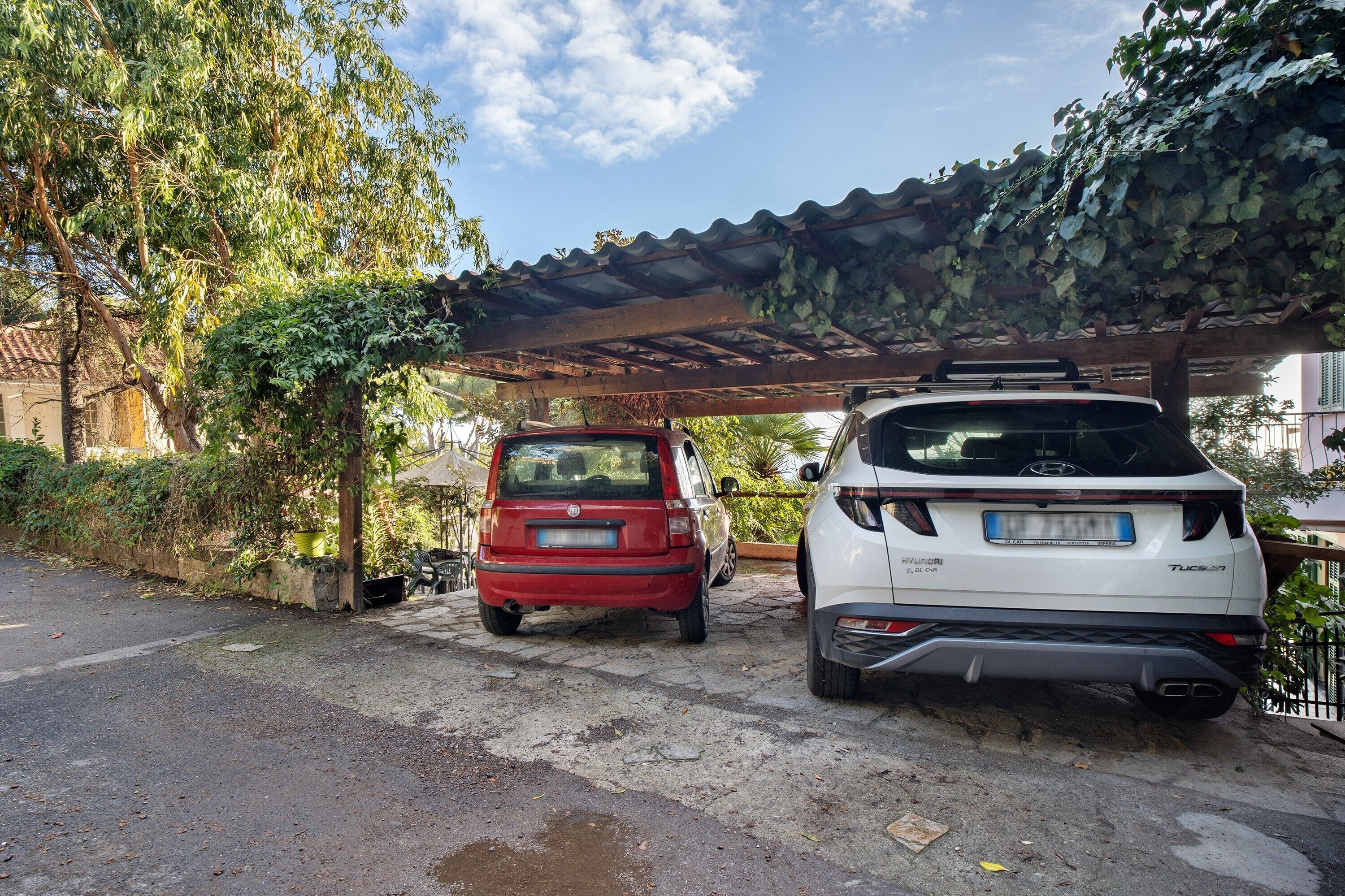 Two parked cars under a covered area with a roof and a tree nearby.