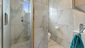 A bathroom with a glass shower enclosure, a toilet, and a sink with a towel hanging on the wall. - 11 of 43 woodward road mount albert (Auckland)