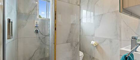 A bathroom with a glass shower enclosure, a toilet, and a sink with a towel hanging on the wall.