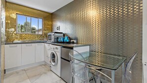 A modern kitchen with a washing machine, microwave, and toaster, a glass table, and a patterned backsplash. - 11 of 43 woodward road mount albert (Auckland)