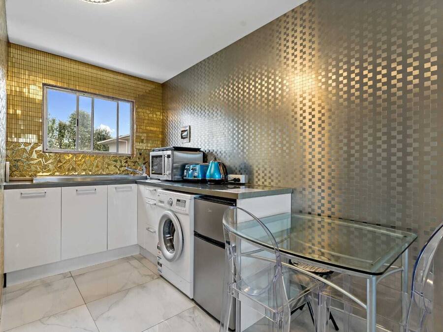 Een moderne keuken met een wasmachine, magnetron en broodrooster, een glazen tafel en een decoratieve spatwand.