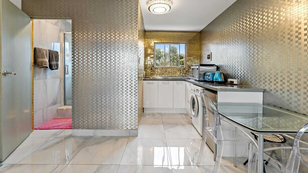 A modern kitchen with a washing machine, a glass table, and a view of the outdoors. - 11 of 43 woodward road mount albert (Auckland)
