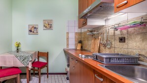 Eine kleine Küche mit Holdelementen, einem Edelstahl-Spülbecken und einer gefliesten Spritzschutzwand. Ein Esstisch mit einem Stuhl und einer Blumenvase stehen dort.