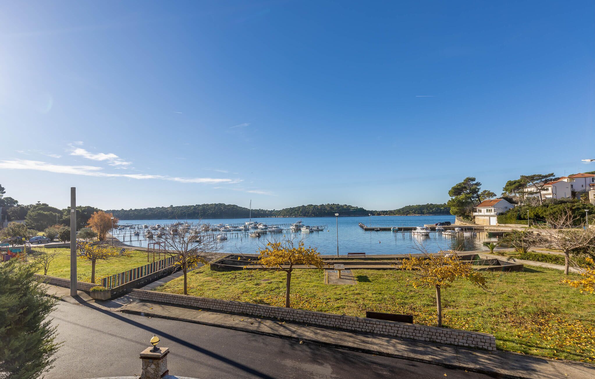 En lystbådehavn med fortøjede både, en klar himmel og et bakket landskab i baggrunden.