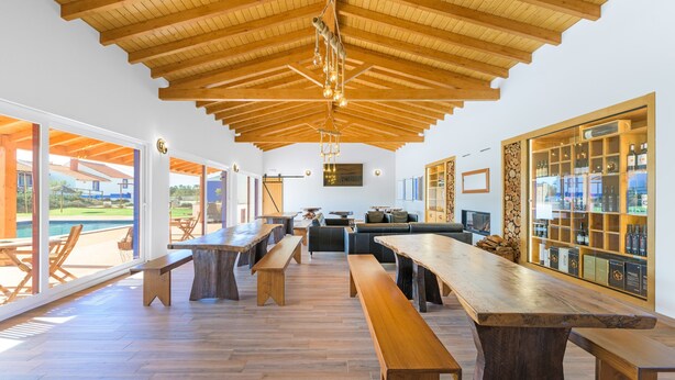 A spacious indoor area with wooden benches, a high ceiling with exposed beams, and a view of the outdoors through large glass doors. - Holiday Home 'Clarinha' with Mountain View, Wi-Fi and Air Conditioning (Odemira)
