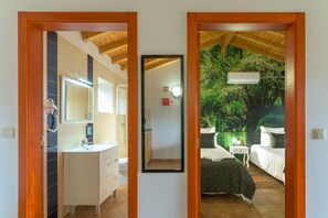 A room with a bathroom, a mirror, a bed with a patterned bedspread, and a nightstand with a lamp.