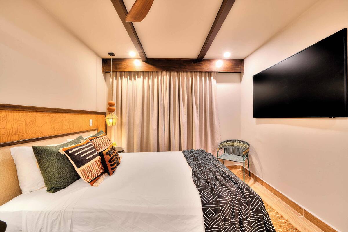 Ein modernes Hotelzimmer mit einem großen Bett, einem flachbildfernseher an der Wand, einer Holzbalkendecke und einem Fenster mit Vorhängen.