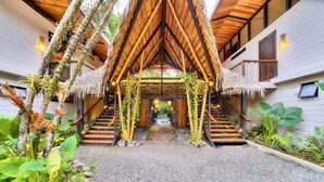 A covered outdoor staircase with wooden railings and a thatched roof, surrounded by tropical plants. - Conga Boutique Hotel (Cahuita)