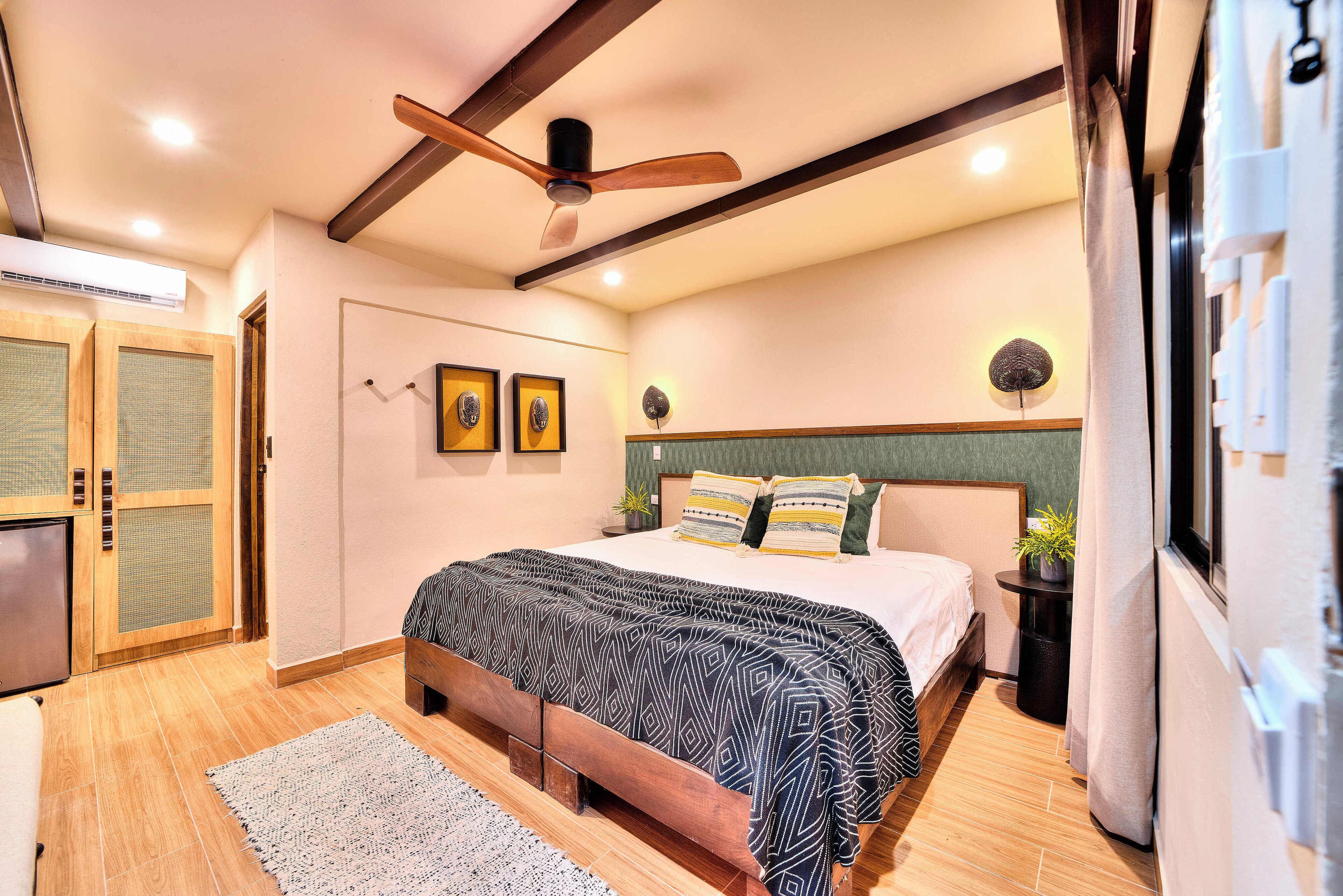 Un dormitorio con cama, suelo de madera, ventilador de techo y una pequeña planta en maceta.