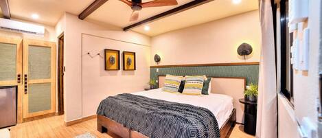 Un dormitorio con cama, suelo de madera, ventilador de techo y una pequeña planta en maceta.