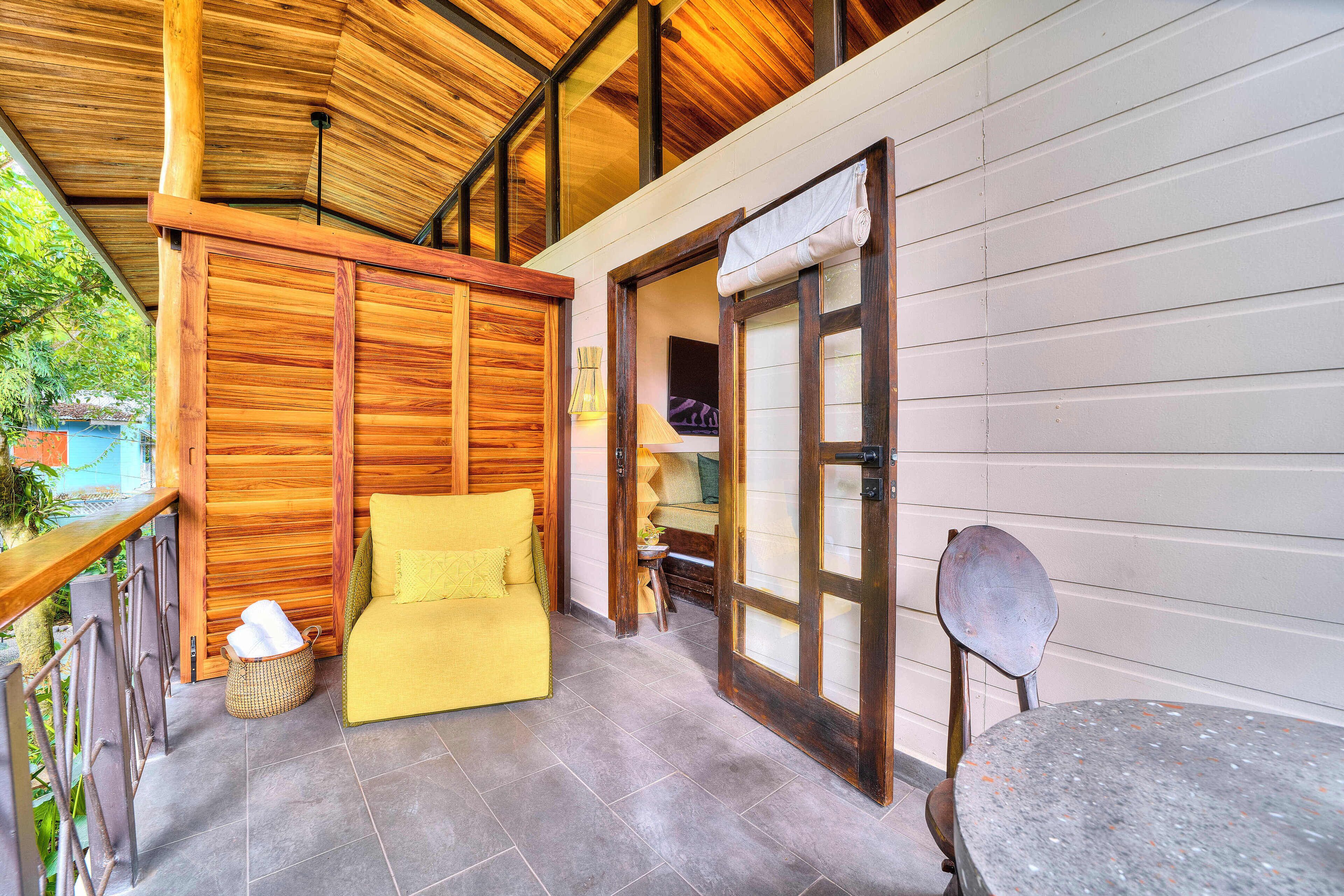 A wooden ceiling, a yellow sofa, a table, and a chair in a room with a view.