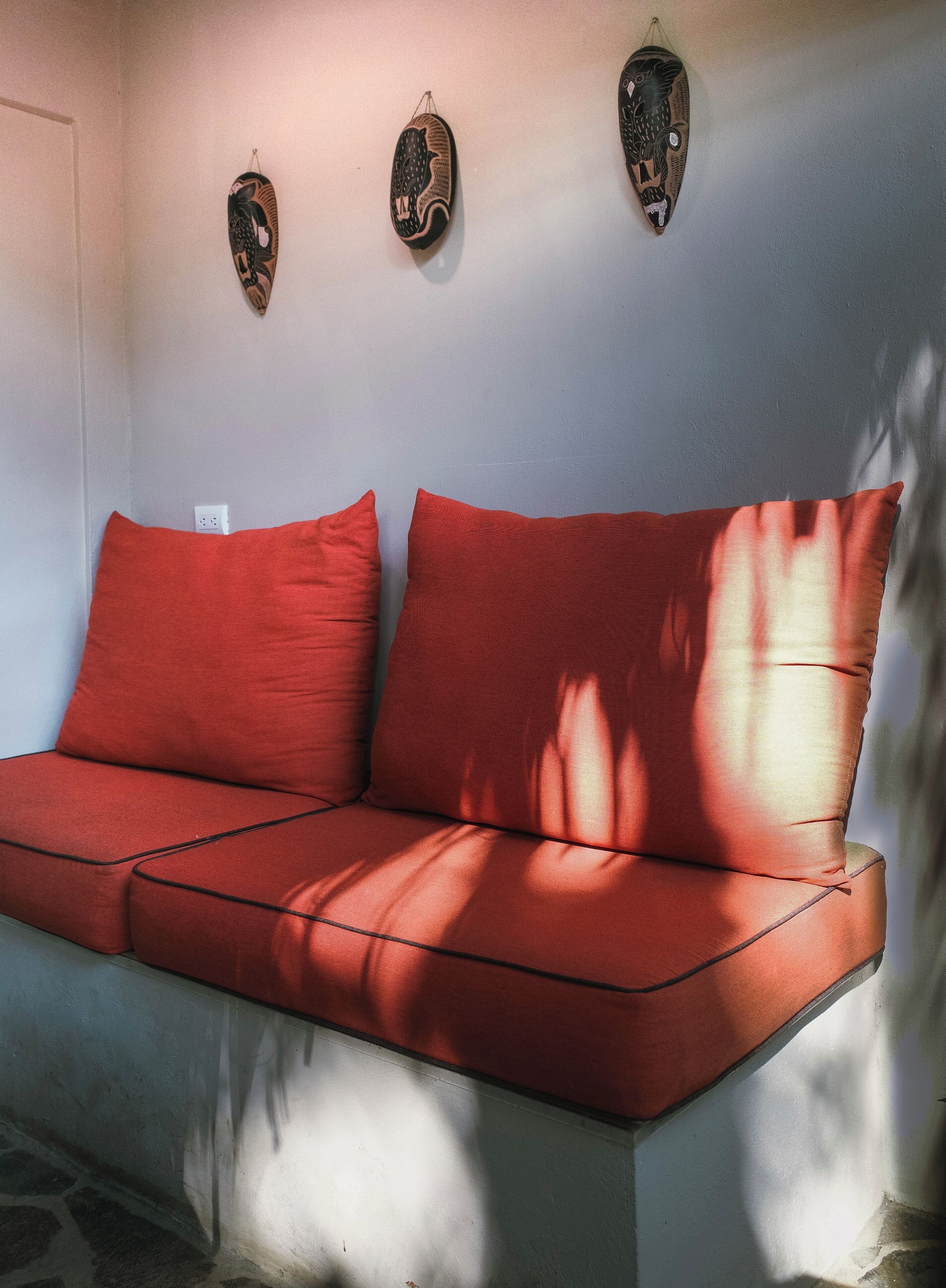 Un sofá rojo con una pared blanca y tres adornos colgados en la pared.