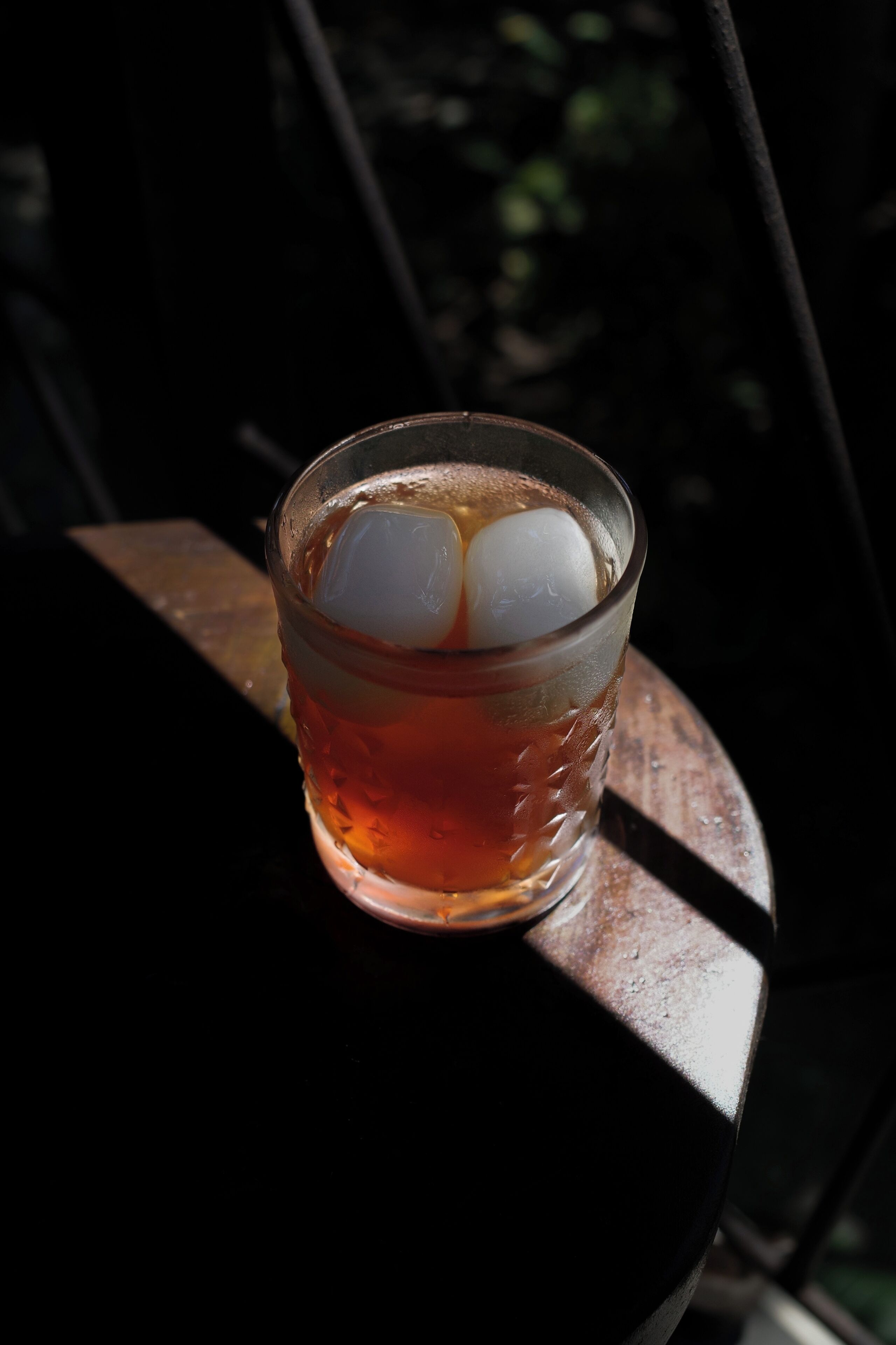 A glass with a beverage and ice cubes on a wooden surface.