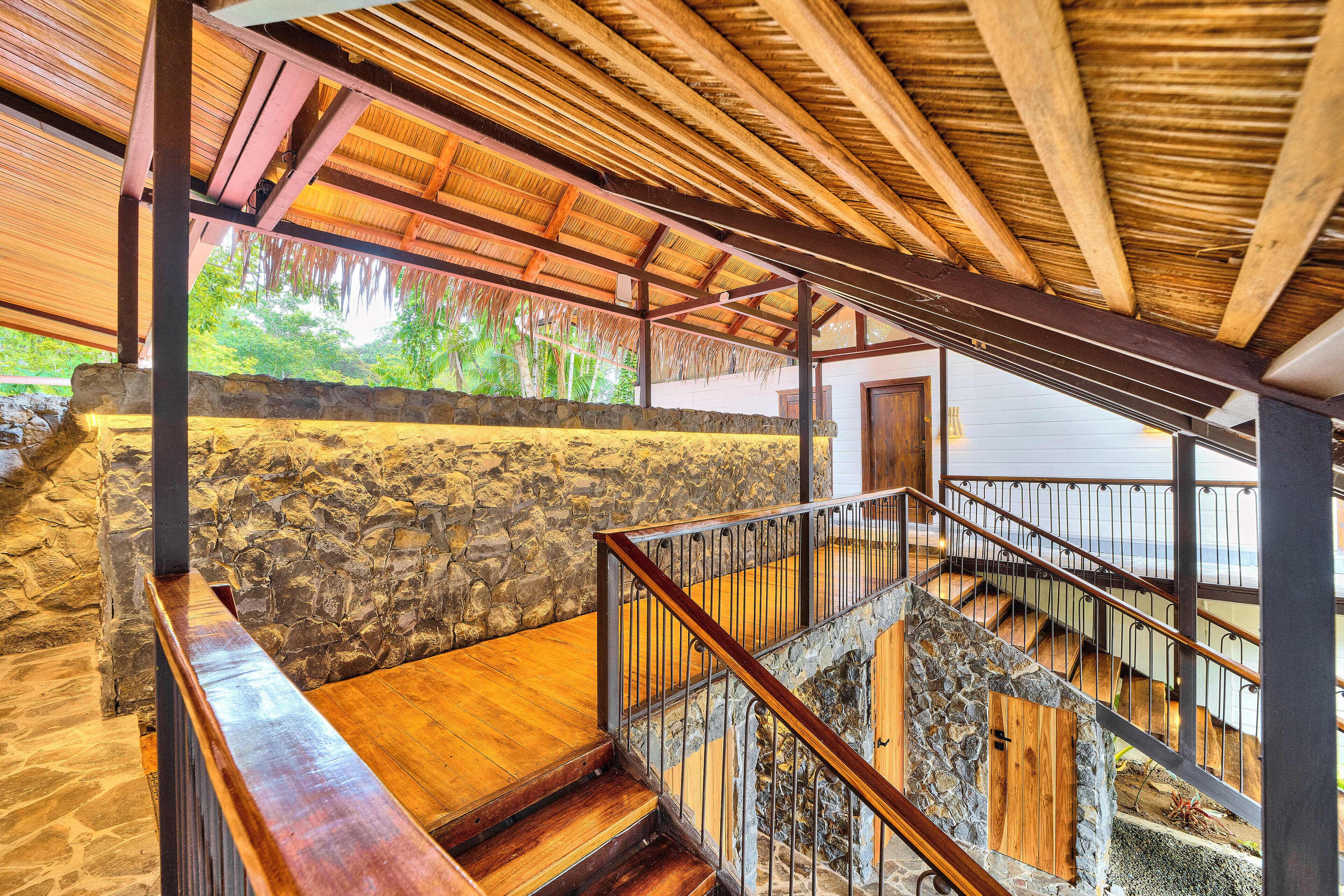 A wooden staircase with stone walls and a metal railing, leading to an upper level with a view of the outdoors.