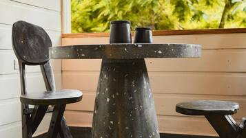 A table with two black chairs, a pendant light, and a view of greenery outside.