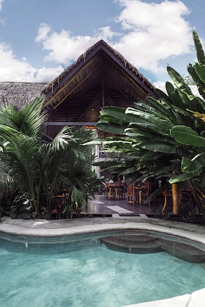 Relax by the tranquil pool surrounded by lush tropical plants and a serene water feature.