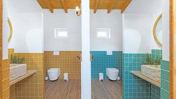 Une salle de bain avec un plafond en bois, deux toilettes, un lavabo agrémenté d’une plante et un miroir.