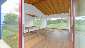 Een interieur met een houten plafond, grote ramen en yogamatten op de vloer.