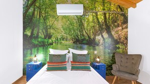 Een slaapkamer met een muurschildering van een rivier in een bos, een bed met witte lakens, twee nachtkastjes met lampen en een stoel.