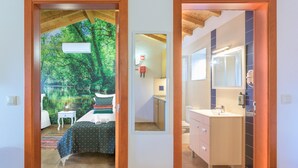 A bedroom with a bed, bedside table, and a view of a forest through a window.