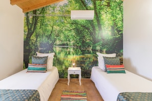 Habitación con dos camas, una mesita de noche, aire acondicionado y un mural temático de bosque.