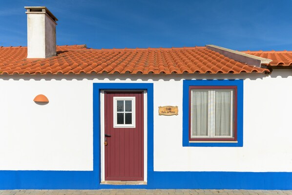 Un bâtiment blanc avec une porte rouge, une fenêtre avec un rideau et des bordures bleues.