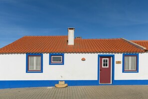 Un bâtiment à deux étages, avec un toit recouvert de tuiles rouges, une façade blanche et bleue, et un petit porche.