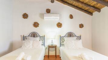 A room with two beds, a small table, an air conditioning unit, and decorative wall plaques.