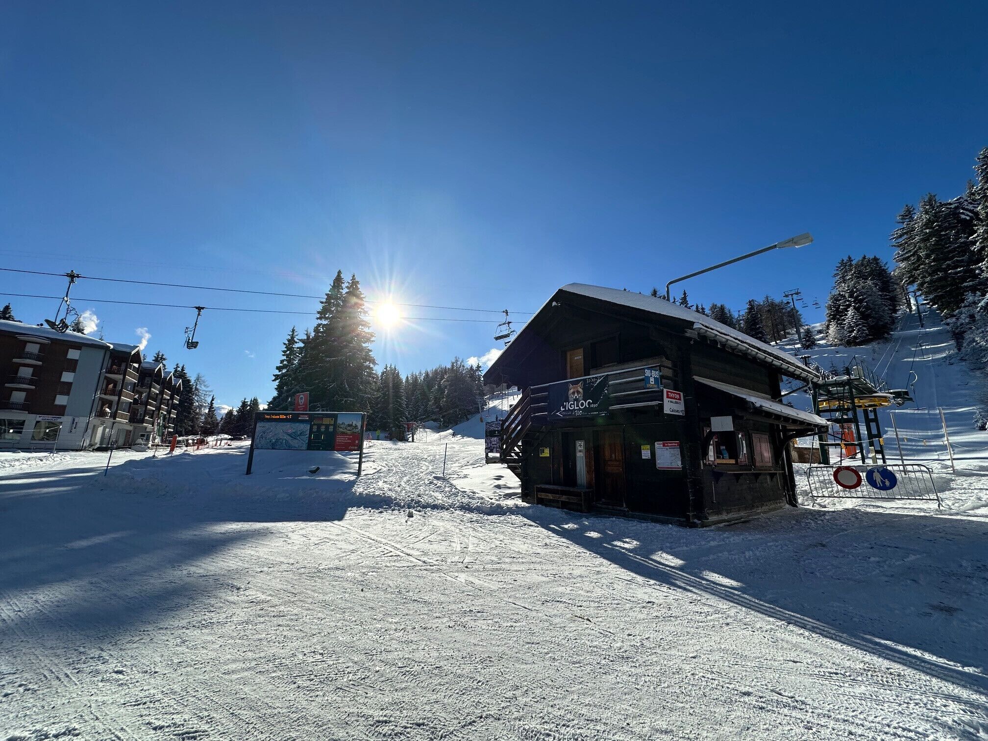 A snow-covered ski resort with a wooden lodge, ski lifts, and a clear blue sky.