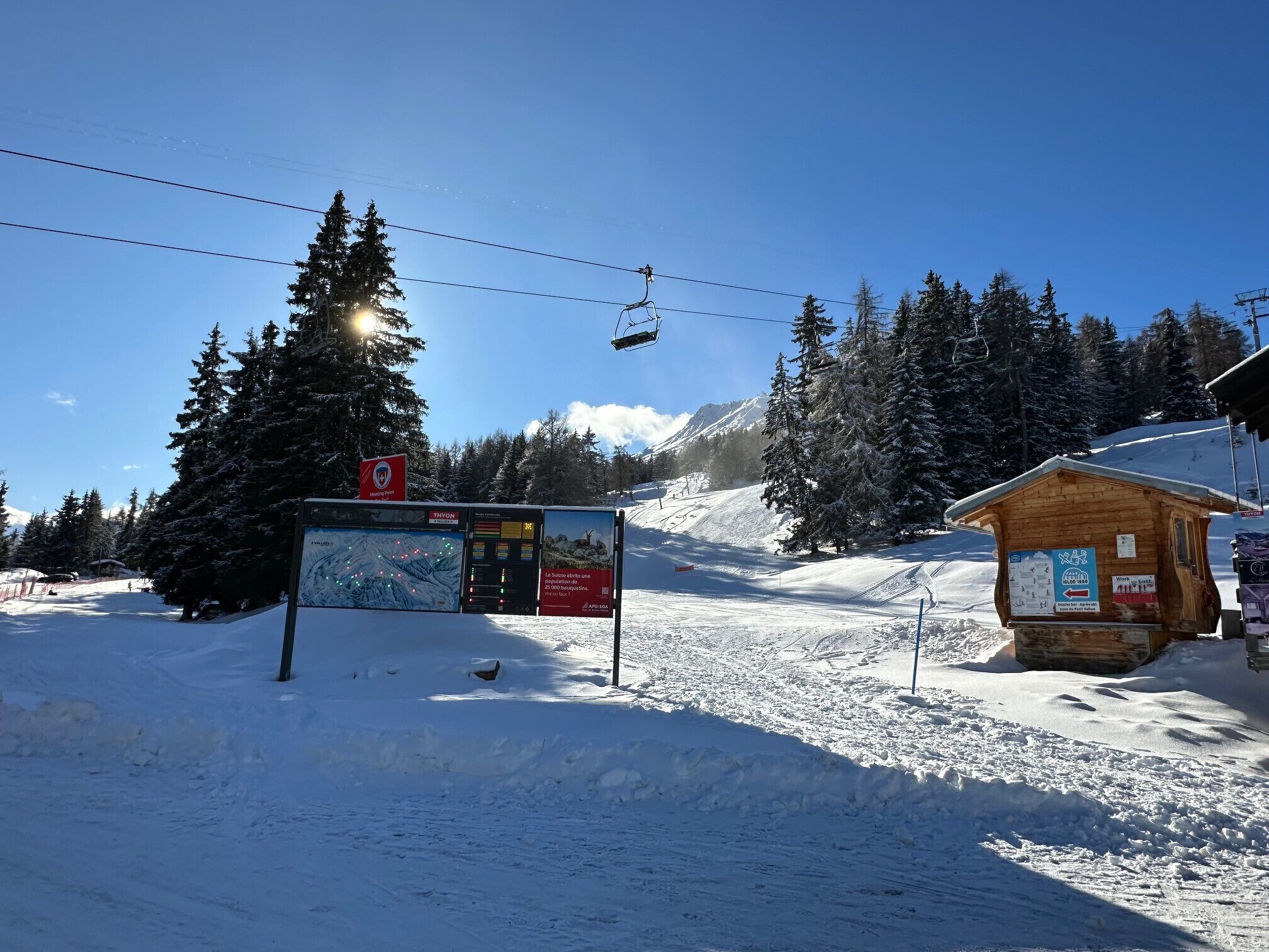 A ski resort with a wooden cabin, a ski lift, and a signboard with information.