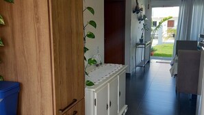 A hallway with a wooden wardrobe, a white console table with plants, a blue trash bin, and a view of the outside through a glass door. - Casa Harmonia do Litoral - Florianopolis (Florianópolis)