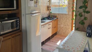 A modern kitchen with a refrigerator, microwave, and oven. There is a window with a view of the outside, and a plant on the right side. - Casa Harmonia do Litoral - Florianopolis (Florianópolis)