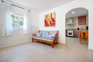 Ein Zimmer mit einer Couch, einem Gemälde, einem Fenster mit Vorhängen und einer Küchenzeile.