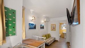 Une cuisine compacte avec un évier, une table en bois et des chaises blanches. Un canapé avec des coussins verts est placé contre le mur.