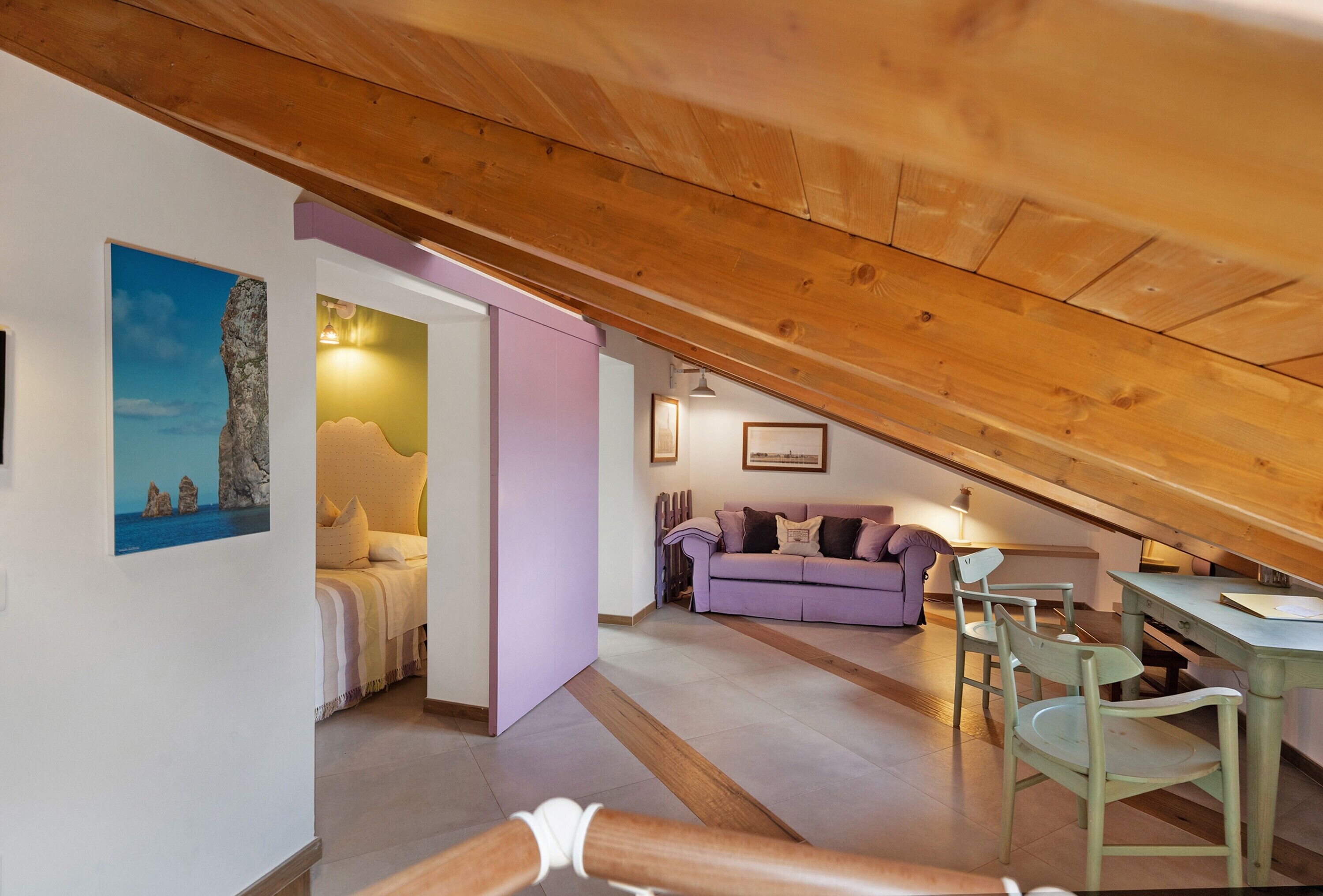 A loft-style room with a sloped ceiling, a bed, a purple sofa, and a dining table with chairs.