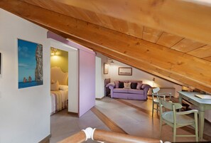 Ett rum i loftstil med ett sluttande tak, en säng, en lila soffa och ett matbord med stolar.