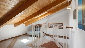 Un plafond en bois à pente douce, un escalier avec une rampe blanche et un luminaire.